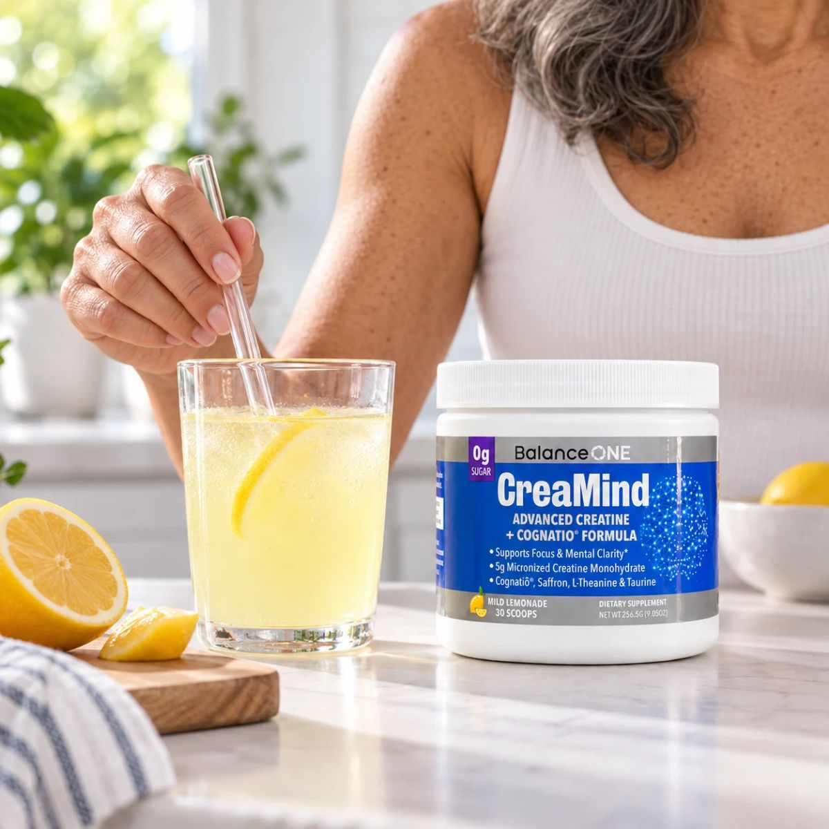 Mature woman stirring a glass of lemonade beside a tub of CreaMind